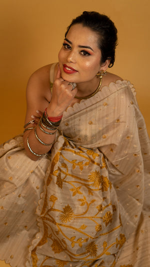 Beige tissue silk saree with golden floral embroidery and scalloped designer border